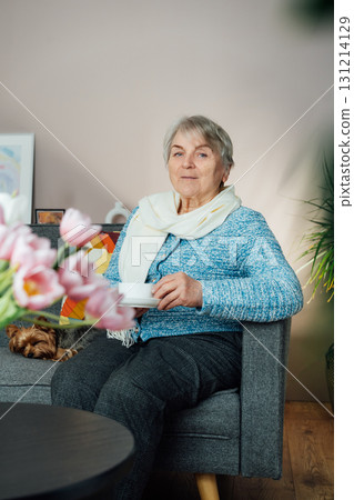 Smiling mature woman with dog pet relaxing at home with cup of tea, positive senior sitting on couch in modern living room looking satisfied feels good, older generation happy retired time enjoy life 131214129