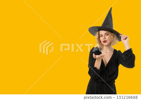 A festive witch blows kisses while wearing a black dress and hat 131216688
