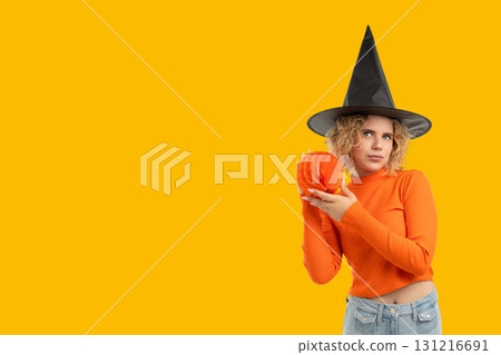 Witch dressed in orange holds a pumpkin against bright backdrop Witch dressed in orange holds a pumpkin against bright backdrop 131216691