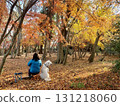 An owner and a large white dog sitting on a chair in a forest at the peak of autumn foliage 131218060