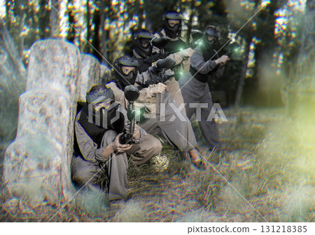 Group of paintball players aiming and shooting with guns outdoors Group of paintball players aiming and shooting with guns outdoors 131218385