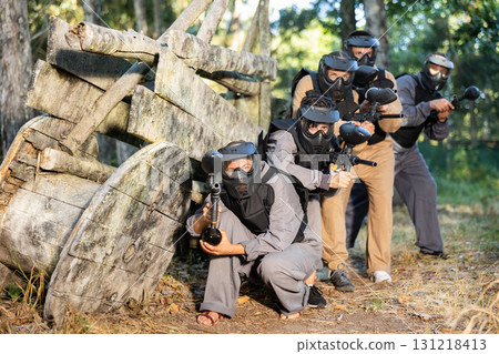 Paintball players of one team in camouflages and masks aiming with gun in shootout 131218413