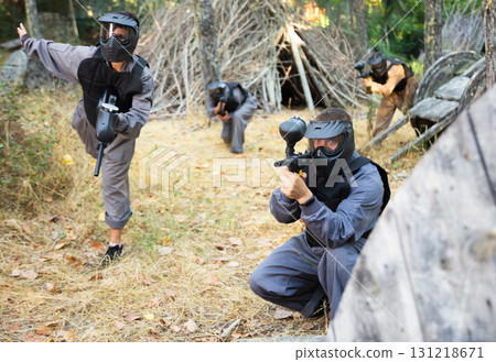 Team of positive smiling people playing paintball on battlefield outdoor, running with guns 131218671