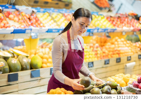 Female salesperson carefully places ripe avocado fruit on the counter of grocery supermarket Female salesperson carefully places ripe avocado fruit on the counter of grocery supermarket 131218730