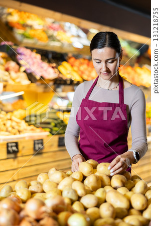 Middle-aged female seller putting potatoes on counter in grocery market 131218755