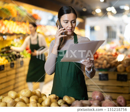 Woman seller takes inventory and talks on phone in vegetable shop Woman seller takes inventory and talks on phone in vegetable shop 131218756