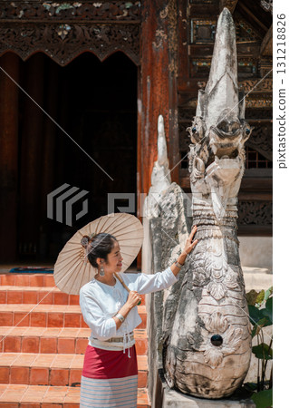 A woman in traditional attire with a parasol admires a detailed stone sculpture at an ancient temple. 131218826