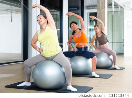 Women exercising with ball during group pilates class Women exercising with ball during group pilates class 131218844