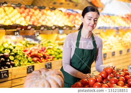Middle-aged female seller putting tomatoes on counter in grocery market Middle-aged female seller putting tomatoes on counter in grocery market 131218851