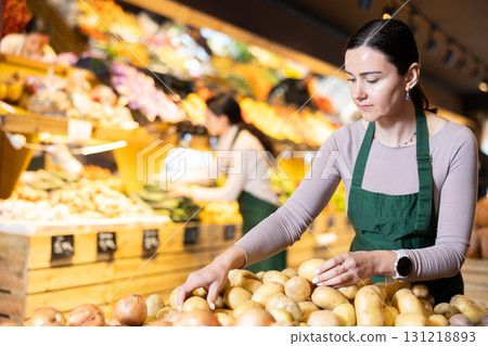 Female seller laying out potatoes on the counter 131218893