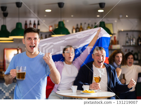 Happy friends of different ages drinking beer and celebrating the victory of the Russian team in night bar 131219007