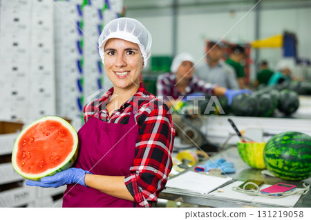Smiling workwoman of fruit sorting factory standing with half of watermelon Smiling workwoman of fruit sorting factory standing with half of watermelon 131219058