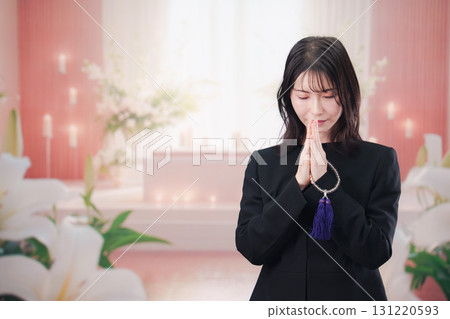 A young woman wearing mourning clothes and praying at a funeral or wake 131220593