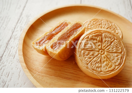 A photo of Japanese sweets, monaka, with citrus-patterned skins and densely packed bean paste, arranged in a wooden dish A photo of Japanese sweets, monaka, with citrus-patterned skins and densely packed bean paste, arranged in a wooden dish 131222579