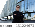 Confident man posing near modern glass building in urban setting during daylight hours 131224673