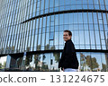 Man smiling in front of modern glass building during sunny day in urban area 131224675