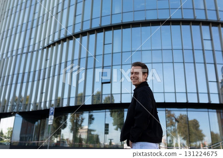 Man smiling in front of modern glass building during sunny day in urban area 131224675