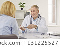 Mature male doctor sitting at his office and consulting female patient 131225527