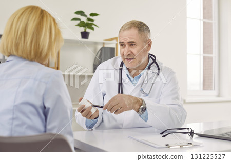 Mature male doctor sitting at his office and consulting female patient 131225527