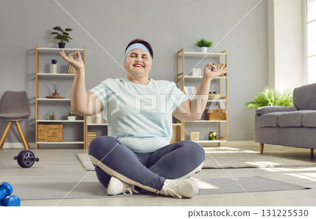 Fat woman relaxing sitting on yoga mat with closed eyes in Lotus pose at home. Fat woman relaxing sitting on yoga mat with closed eyes in Lotus pose at home. 131225530