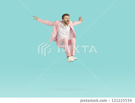 Funny excited man wearing stylish pink suit jumping isolated on studio blue background. 131225534