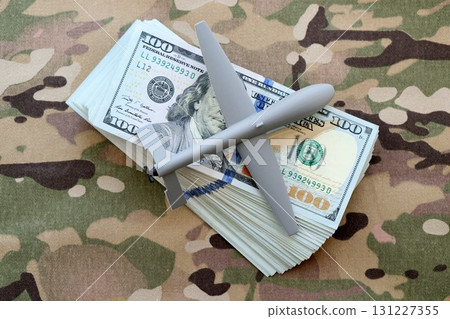 Unnamed grey toy drone model and dollar bills on camouflage fabric. Drone manufacturing funds 131227355