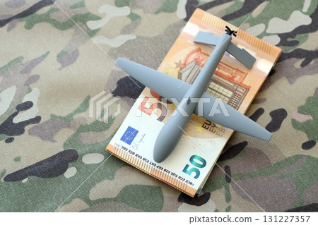 Unnamed grey toy drone and Euro money bills on camouflage fabric close up Unnamed grey toy drone and Euro money bills on camouflage fabric close up 131227357