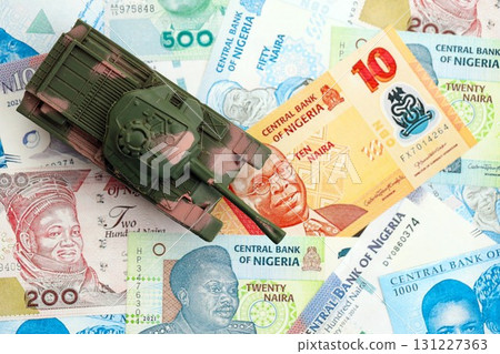 Nigerian naira currency money bills and toy tank. The concept of army funds and weapons sales Nigerian naira currency money bills and toy tank. The concept of army funds and weapons sales 131227363
