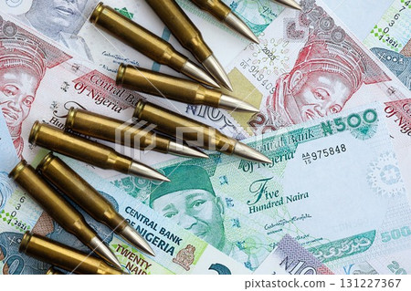 Nigerian naira currency money bills and rifle bullets. The concept of warfare and gun selling Nigerian naira currency money bills and rifle bullets. The concept of warfare and gun selling 131227367