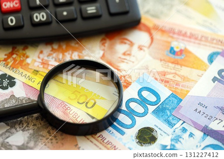 Philippines peso currency money bills and calculator with magnifying glass. The concept of taxation and money count Philippines peso currency money bills and calculator with magnifying glass. The concept of taxation and money count 131227412