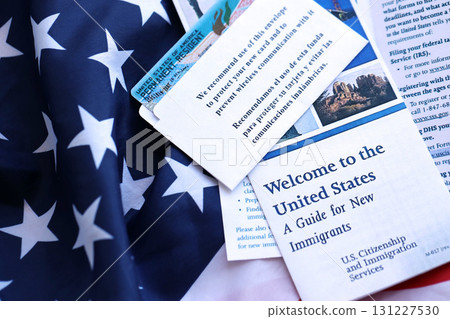 Permanent resident green card in envelope and guide for new immigrants lies on US flag Permanent resident green card in envelope and guide for new immigrants lies on US flag 131227530
