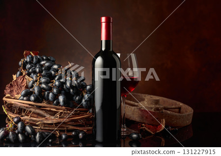 Glass and bottle of red wine with blue grapes on a black reflective background. Glass and bottle of red wine with blue grapes on a black reflective background. 131227915