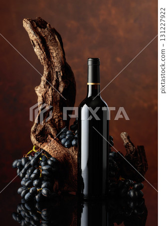 Bottle of red wine with an old snag and blue grapes. Bottle of red wine with an old snag and blue grapes. 131227922