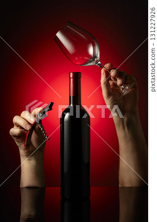 Unopened bottle of red wine and hands with corkscrew and wine glass. 131227926
