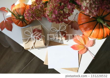Cozy autumn flat lay with two wrapped gifts, pumpkins, fall leaves and an empty greeting card on white surface. Perfect for seasonal celebrations and Thanksgiving 131228532