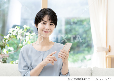 坐在沙發上使用智能手機的年輕女性 坐在沙發上使用智能手機的年輕女性 131229762