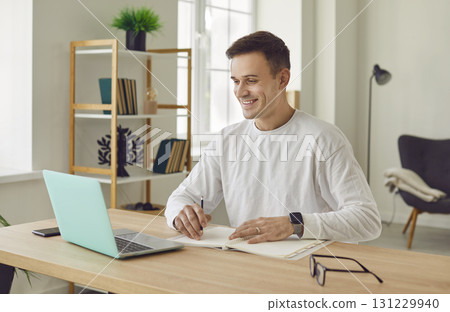 Portrait of young attractive business man working on a laptop and looking cheerful at camera. Portrait of young attractive business man working on a laptop and looking cheerful at camera. 131229940
