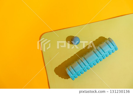 Top view corner of yoga mat with massage ball and foam roller casting long shadows on yellow bright studio 131230136