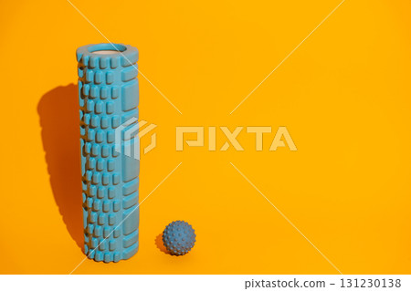Vertical foam roller with spiky massage ball on bright yellow minimalist wellness gear copy space Vertical foam roller with spiky massage ball on bright yellow minimalist wellness gear copy space 131230138