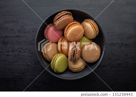 Different flavors of macarons. Colourful macaroons in bowl on black table. Top view. 131230443