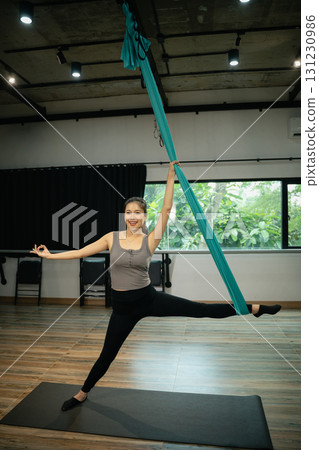 Female athlete balancing with aerial silk, lifting leg sideways during yoga training session 131230986