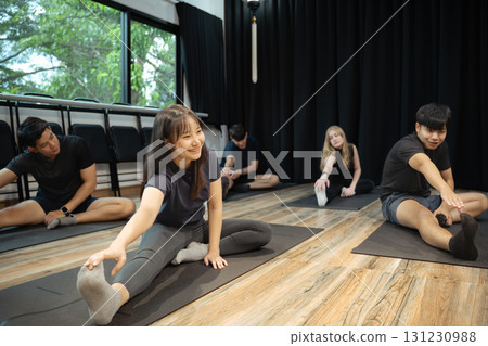 Group of young adults stretching together on yoga mats in a bright fitness studio 131230988