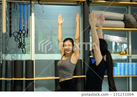 Happy yoga instructor encouraging student during stretching exercise in a bright studio 131231004