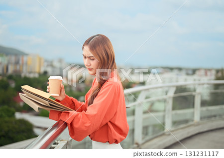 Young businesswoman looking stressed while holding coffee and documents on rooftop city view 131231117