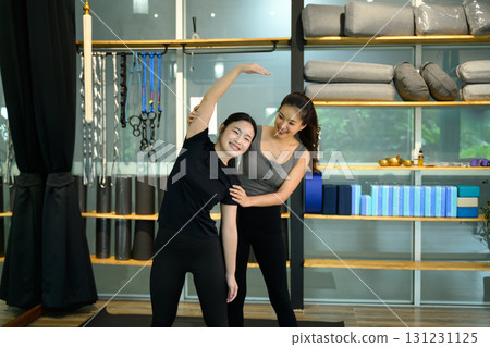 Female trainer assisting young woman with side stretching exercise in a modern yoga studio 131231125