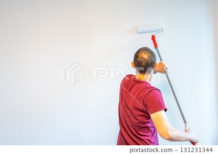 Man painting the wall with an extended roller during home renovation to reach higher surfaces. Concept of efficient interior work, broad coverage and advanced DIY improvement. 131231344