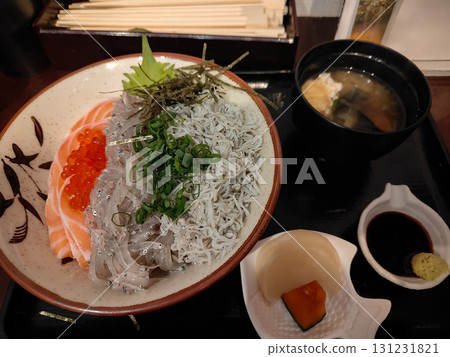 A Japanese meal set with a rice bowl topped with raw salmon, tiny fish, and salmon roe, served with miso soup and pickles. Fresh toppings and side dishes highlight a traditional dining experience in 131231821