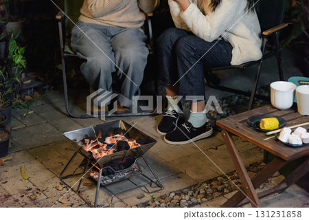 Winter camp outdoor friends women happy, warm cozy forest setting features portable grill charcoal glowing, winter evening gathering enjoy roasting food marshmallows corn. 131231858