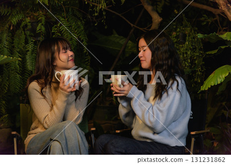 Winter camp outdoor, happy woman friend people enjoy forest evening, holding warm mugs, conversing comfortably, creating peaceful leisure time and cozy winter gathering memories. 131231862