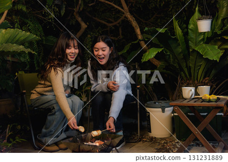 Winter camp outdoor friend people woman happy in forest, two women enjoy roasting marshmallows over warm glowing fire during cozy winter evening experience. 131231889